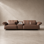 A modern two-seater sofa in brown leather with a central side table, set against a minimalist textured beige wall and concrete floor.